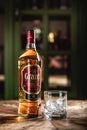 GrantÃ¢â¬â¢s whiskey bottle and glass with ice cubes on wooden table in dark bar